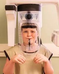 A young patient standing in the digital panoramic X-ray machine at Sicher Family Dentistry.