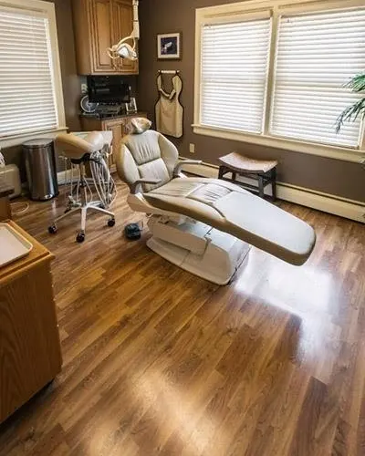 A treatment room at Sicher Family Dentistry, with a dental chair, wood floor and window blinds.